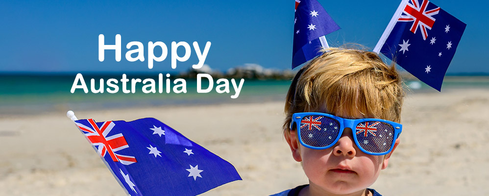 Cute smiling kid with flags of Australia sitting on the sand at the beach